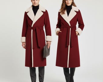 May include: Two people wearing matching burgundy long coats with cream-colored faux fur collars and cuffs. The coats have a belted waist and are knee-length. One person holds a dark gray clutch. The background is plain white.