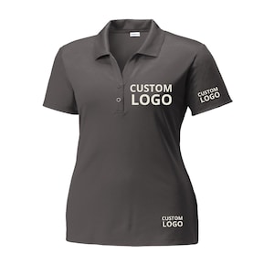 May include: A charcoal gray polo shirt with short sleeves and a collared neckline. The shirt features the text "CUSTOM LOGO" in white on the chest, sleeve, and lower front.