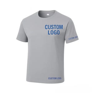 May include: A light gray t-shirt with the words "CUSTOM LOGO" printed in blue on the chest, sleeve, and lower front. The shirt has a crew neck and short sleeves. The fabric appears to be a lightweight, breathable material.