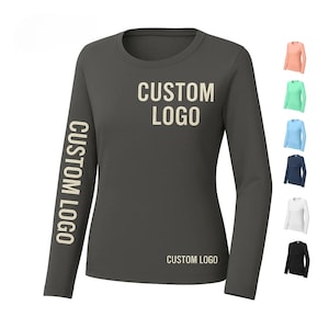 May include: A charcoal gray long-sleeve shirt with the text "CUSTOM LOGO" printed on the left sleeve, front, and bottom. Additional color options are displayed on the right side, including peach, mint green, light blue, navy, white, and black.