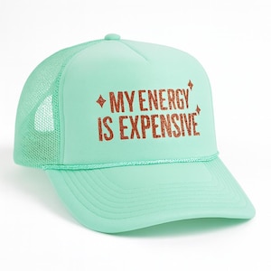 May include: A mint green trucker hat with a mesh back and a curved brim. The hat features the text "MY ENERGY IS EXPENSIVE" in glittery copper-colored letters. The hat has a rope detail along the front.
