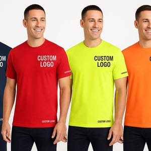 K&ouml;nnte beinhalten: Vier kurz&auml;rmelige T-Shirts in Marineblau, Rot, Neongelb und Orange. Jedes Shirt tr&auml;gt den Text "CUSTOM LOGO" auf der Brust und am unteren Saum. Die Shirts werden von einer Person getragen.