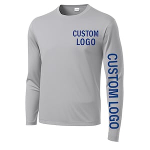 May include: A light gray long-sleeve shirt with the text "CUSTOM LOGO" printed in blue on the chest and down the right sleeve. The shirt has a crew neck and is made of a smooth, likely athletic material.