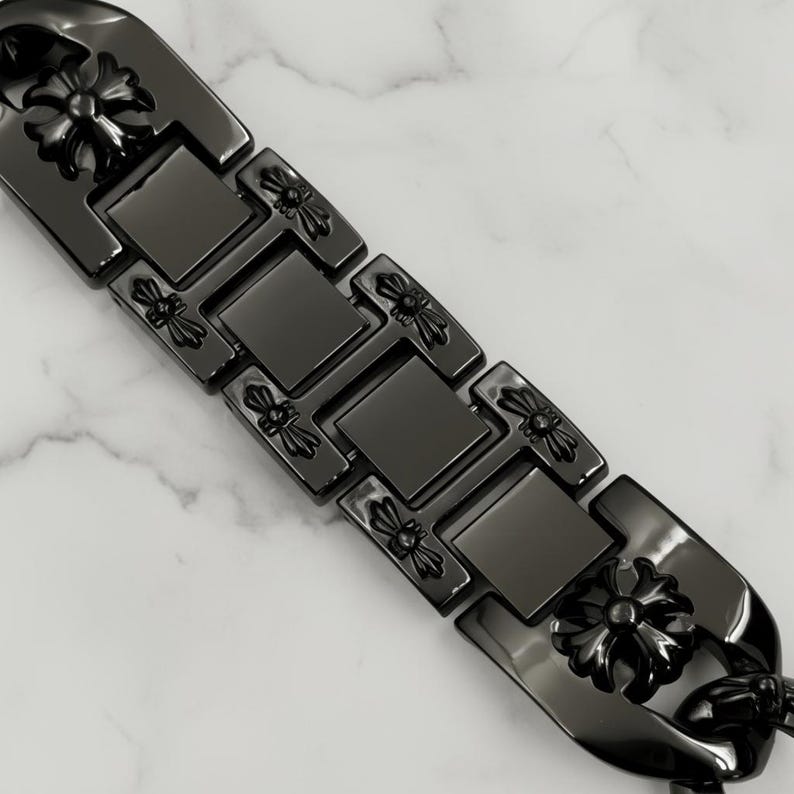以下が含まれることがあります： 黒いブレスレットのクローズアップ。フローラルデザイン。ブレスレットは長方形と正方形のリンクでできており、各リンクに装飾的なフローラル要素があります。ブレスレットは白とグレーの大理石の表面にあります。