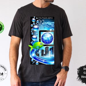 May include: Dark grey heather t-shirt featuring a vibrant graphic. The design includes a digital illustration with a globe, city skyline, and a green and yellow fish. The text "FRUTIGER AERO" is at the top.