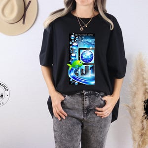 May include: Black t-shirt featuring a vibrant graphic with a fish, globe, and city skyline design. The design incorporates blue and green hues, with the text "FRUTIGER AERO" at the top. The shirt is a casual wear item.