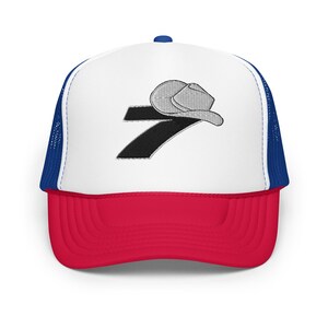 May include: A white and red trucker hat with a blue mesh back. The front of the hat features a black number 7 with a gray cowboy hat on top.