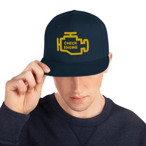 May include: A navy blue baseball cap with a yellow check engine light graphic and the text "CHECK ENGINE".