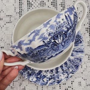 以下が含まれることがあります： 馬車に乗った狩猟のシーンが描かれた青と白の磁器製のスープボウルとソーサーのセット。セットは波状の縁取りと繊細な花柄が施されています。