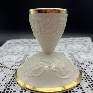 May include: A white porcelain candle holder with a gold trim and an embossed floral design.