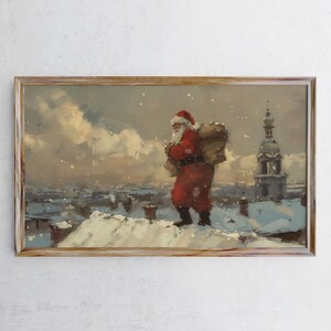 May include: A framed painting depicts Santa Claus in a red suit and hat, carrying a large sack over his shoulder. He walks across a snow-covered rooftop, with a cityscape and falling snow in the background. The artwork has a vintage, painterly style.