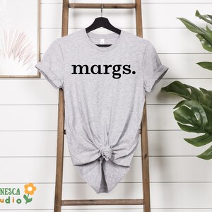 Pu&ograve; includere: Una maglietta grigia con la parola "margs." stampata in nero sul davanti.