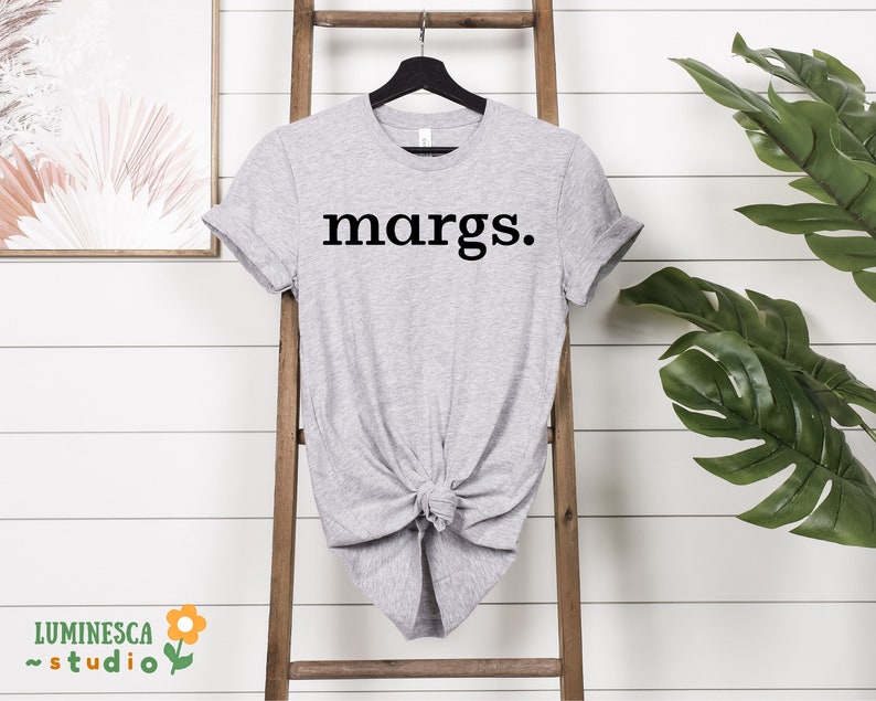 Pu&ograve; includere: Una maglietta grigia con la parola "margs." stampata in nero sul davanti.