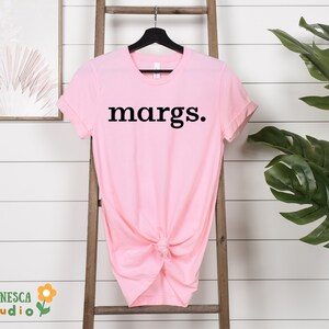 Pu&ograve; includere: Una maglietta rosa con la parola "margs." stampata in nero sul davanti.
