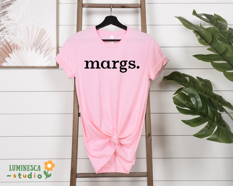 Pu&ograve; includere: Una maglietta rosa con la parola "margs." stampata in nero sul davanti.