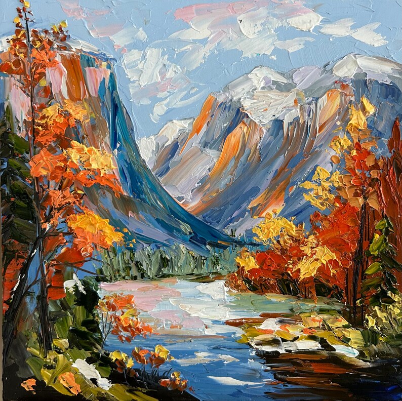May include: An oil painting depicts a mountain landscape with a river. The artwork features a blue sky with white clouds, snow-capped mountains, and trees with orange and yellow foliage. The river reflects the sky and surrounding colors.