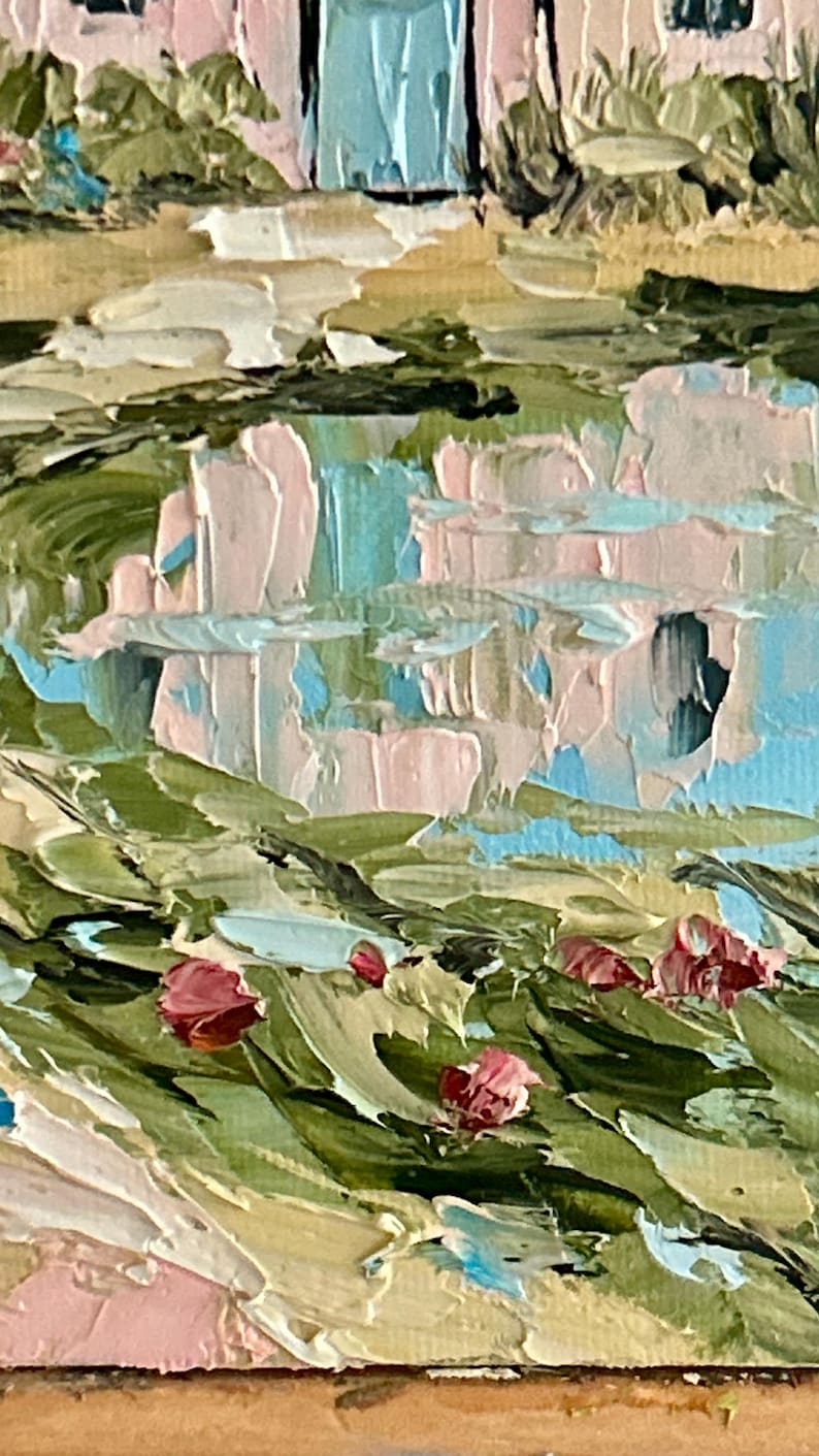 May include: An oil painting featuring thick impasto brushstrokes depicting a pink building with a blue door, reflected in a body of water. The foreground shows green foliage with small red flower buds, rendered in a textured, layered paint style.