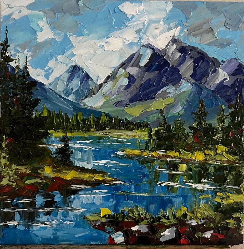 May include: An oil painting depicts a mountain landscape with a lake. The mountains are painted in shades of blue, gray, and purple, with a blue sky and white clouds above. The lake reflects the mountains and sky, with green trees along the shore.