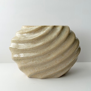 May include: A beige ceramic vase with a wavy, textured design. The vase has a wide opening and a rounded base.