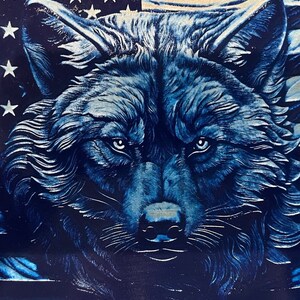 May include: A detailed illustration of a wolf's face in shades of blue. The wolf's fur is textured, and its eyes are a lighter blue. The background features the American flag with white stars and red and white stripes.