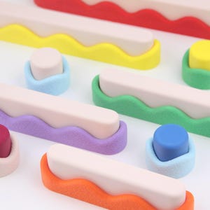 Peut inclure: Ensemble de formes géométriques abstraites et colorées, comprenant du rouge, du jaune, du vert, du violet, de l'orange et du bleu. Les formes semblent être faites d'un matériau doux et texturé, avec une forme rectangulaire beige clair sur le dessus.