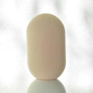 Puede incluir: Un objeto liso de forma ovalada, de color blanco roto, con una superficie texturizada. El objeto est&aacute; sobre una superficie blanca.