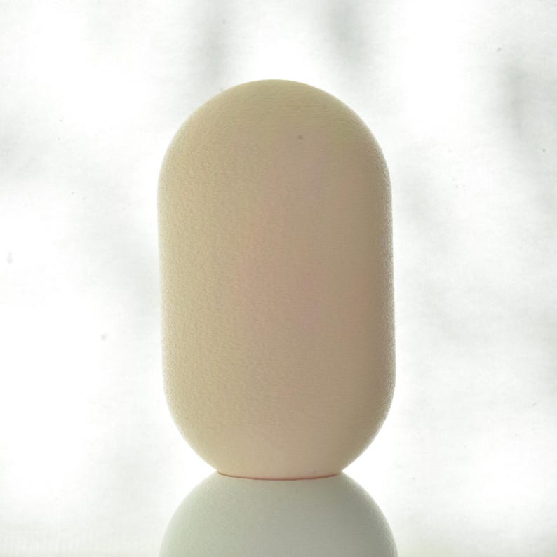 Puede incluir: Un objeto liso de forma ovalada, de color blanco roto, con una superficie texturizada. El objeto est&aacute; sobre una superficie blanca.