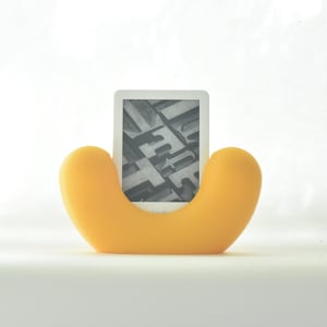 Peut inclure: Un support de lecture électronique jaune avec une liseuse Kindle à l'intérieur. La liseuse affiche une image en noir et blanc d'une page de texte.