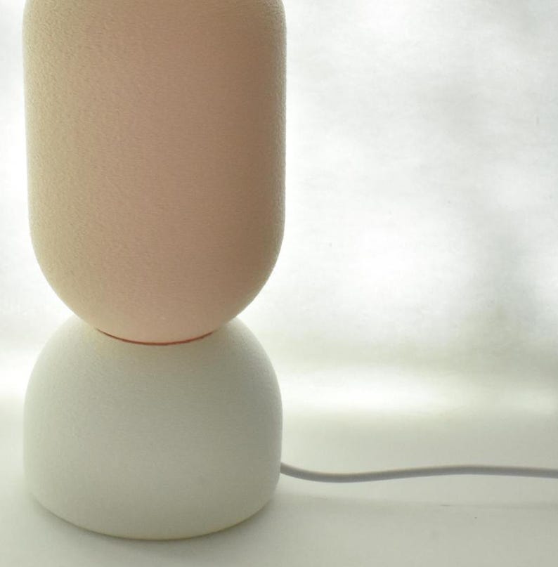 Puede incluir: Una l&aacute;mpara de mesa de cer&aacute;mica blanca y rosa con una base redonda y texturizada y un cable.