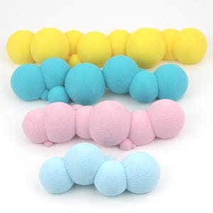 Può includere: Una collezione di forme colorate e strutturate a forma di nuvola in giallo, blu, rosa e azzurro. Le forme sono disposte in file, ognuna composta da più sfere collegate. Lo sfondo è bianco.