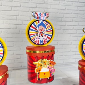 Puede incluir: Adorno para tarta de cumpleaños rojo y amarillo con diseño de personaje de dibujos animados. El adorno presenta el nombre "CARLOS ABDIEL" y la palabra "UNO". El adorno tiene una base roja con ribete dorado.