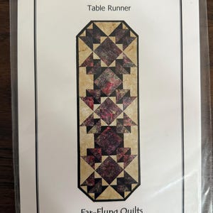 May include: A package for a table runner pattern titled "Moroccan Tiles." The pattern features a geometric design in shades of burgundy, tan, and cream. The package is labeled "Far-Flung Quilts" and includes the website address.