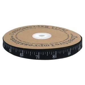 Könnte beinhalten: Schwarzes Baumwollband mit einem weißen, bedruckten Maßband-Design. Das Band ist auf einer braunen Pappspule mit dem aufgedruckten Text "Creative Impressions" und "Teal Expressions" aufgerollt.