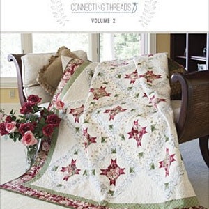 May include: A quilt with a white background and a repeating pattern of red and green stars. The quilt is folded over a light brown chaise lounge with a white pillow and a floral pillow.