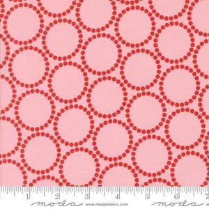 Op de afbeelding: Roze stof met een herhalend patroon van rode gestippelde cirkels. De cirkels overlappen elkaar in een ontwerp. Een liniaal staat onderaan de afbeelding. Het woord "moda" staat op de liniaal.