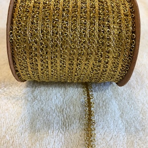 May include: A spool of gold metallic trim with a decorative looped pattern. The trim is wound around a brown cardboard spool.