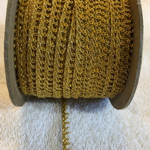 May include: A spool of gold metallic trim with a delicate, intricate design. The trim is wound around a cardboard spool.