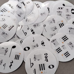 May include: A collection of white, circular music-themed stickers scattered on a gray surface. Each sticker features black musical notes, clef symbols, and piano keys. Some stickers have orange accents.