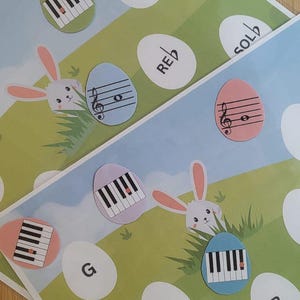 Può includere: Due fogli didattici musicali a tema pasquale. Ogni foglio presenta un coniglietto, note musicali e tasti di pianoforte su uova colorate. Lo sfondo mostra un campo verde e un cielo blu. Sono presenti anche uova bianche con note musicali e lettere.