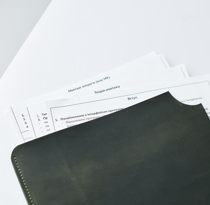 May include: A close-up of a black leather-bound notebook with a yellow stitch along the edge. The notebook is partially covering a white sheet of paper with the text "Монтаж інтерв'ю (міні МК)" and "Теорія монтажу" in black text. The text "Вступ" is also visible in black text.