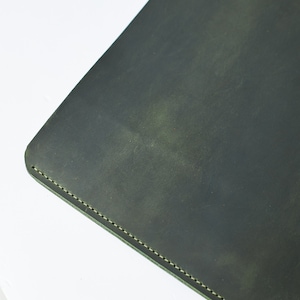 May include: A dark green leather laptop sleeve with a stitched edge.