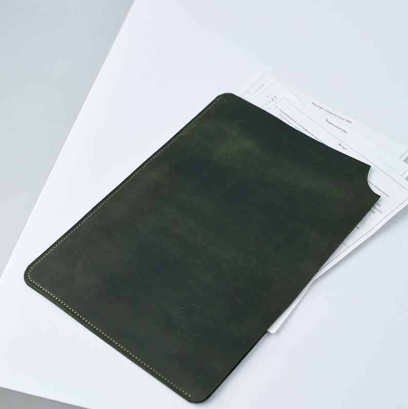 May include: A dark green leather folder with a stitched edge. The folder is open and a white sheet of paper is partially visible.