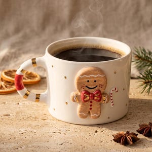 Op de afbeelding: Een witte keramische mok gevuld met donkere koffie, met een 3D peperkoekmannetje met een rode strik en zuurstok. De handgreep heeft rode en gouden strepen. Stoom stijgt op van de koffie.
