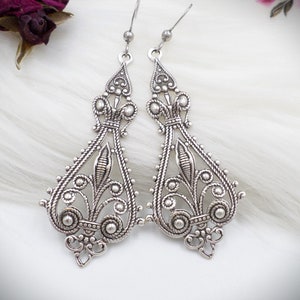 May include: A pair of silver filigree dangle earrings with a teardrop shape and intricate floral designs.