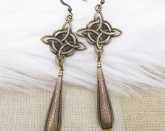 May include: A pair of gold-toned earrings with a Celtic knot design and a teardrop-shaped dangle. The earrings are made of metal and have a polished finish.