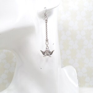 May include: A silver-toned earring featuring a cherub charm with detailed wings and a delicate face. The earring hangs from a twisted metal bar, showcasing a classic design. The earring is displayed on a white surface.