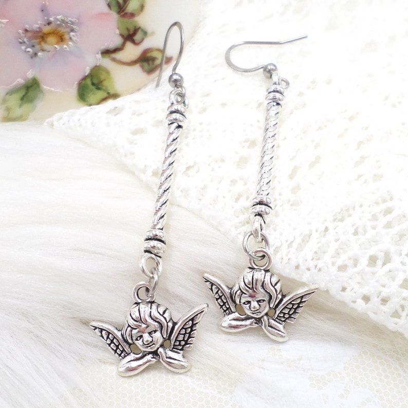 antique silver tone metal cherub angel charms and textured long stick connectors are attached to stainless steel hook style ear wires in these handmade long earrings.