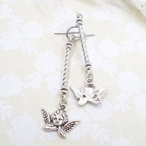 May include: Silver-toned toggle clasp with two dangling charms. One charm is an angel with detailed wings and face, the other is a stylized mask. The clasp has a twisted rope design.