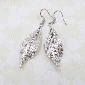 May include: Silver leaf dangle earrings with a textured finish. The earrings have a hook closure.