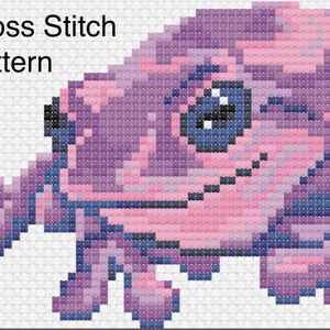 Pode incluir: Padrão de ponto cruz de um sapo roxo com detalhes em rosa e azul. O padrão é intitulado "Cross Stitch Pattern".